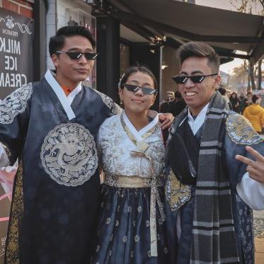 3 students in traditional Chinese garb and pixel sunglasses pose for a picture on a busy street.